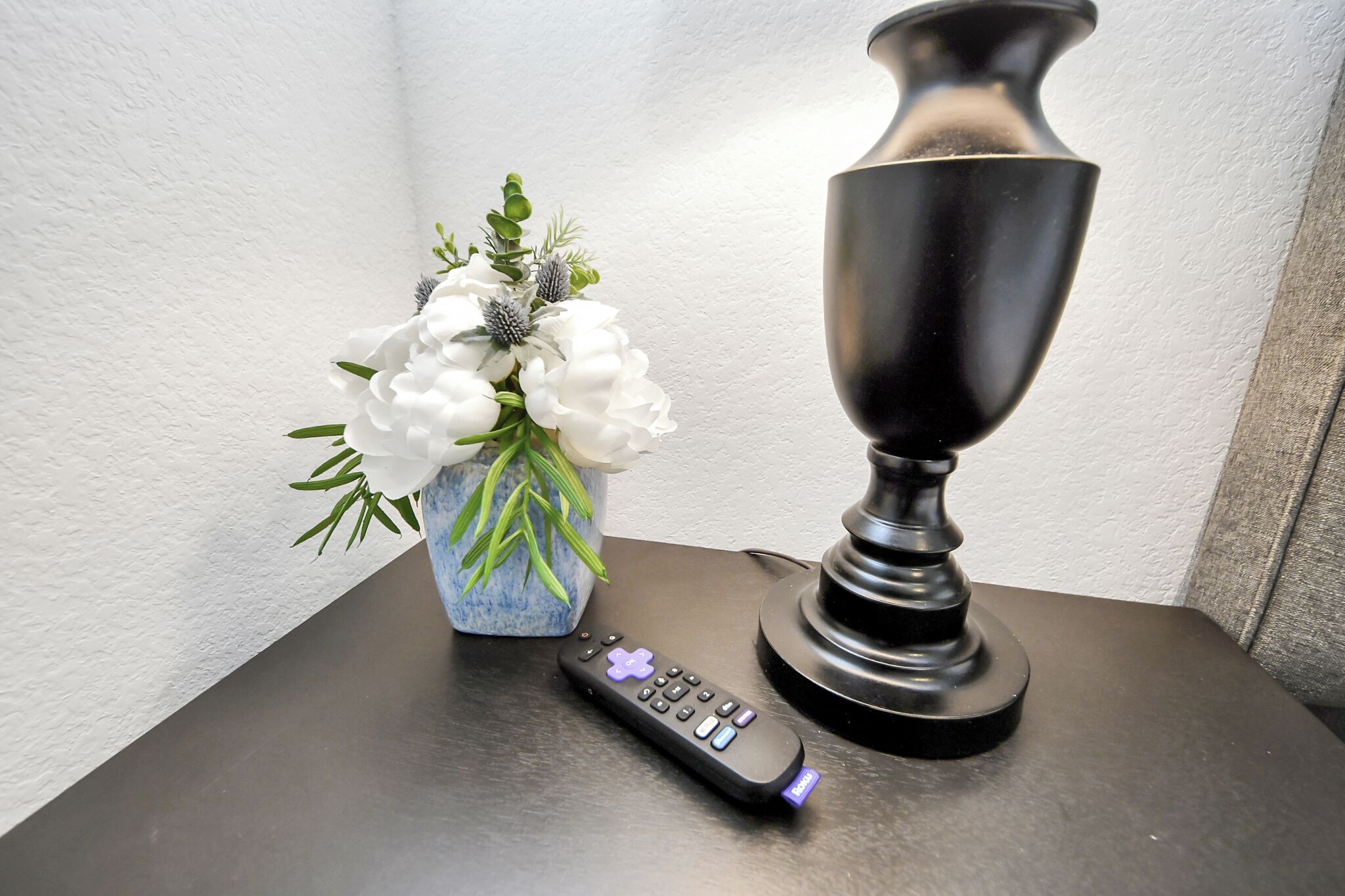 A remote control, a vase with white flowers, and a black lamp on a table.