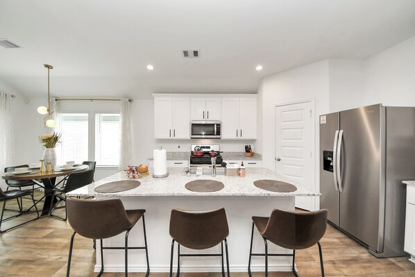 A modern kitchen with white cabinets, a stainless steel refrigerator, and a central island with bar stools.