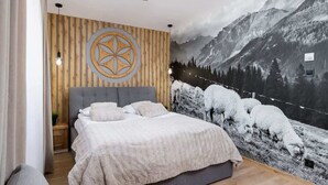 Une chambre à coucher avec un grand lit, un mur en bois orné d’un motif géométrique et une fresque représentant un paysage de montagne.