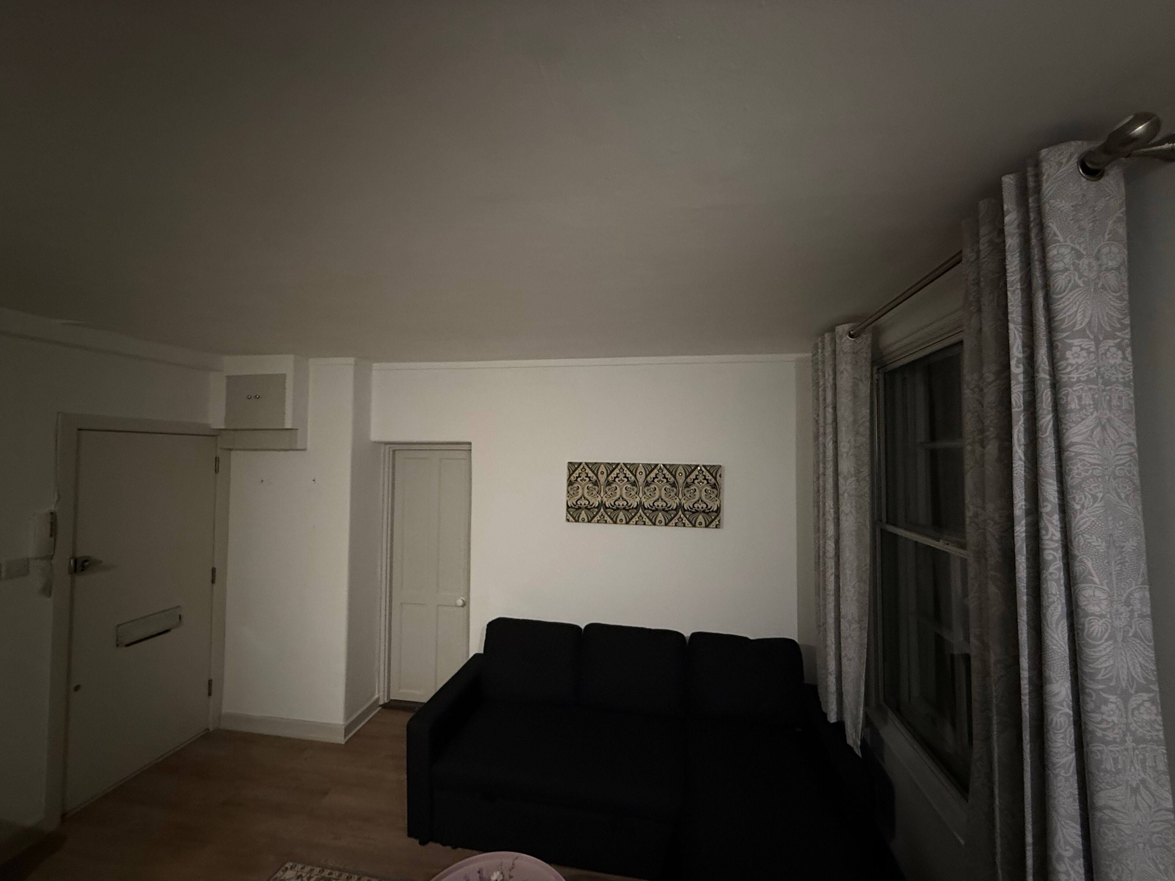 A living room with a black sofa, a patterned wall hanging, and a window with curtains.