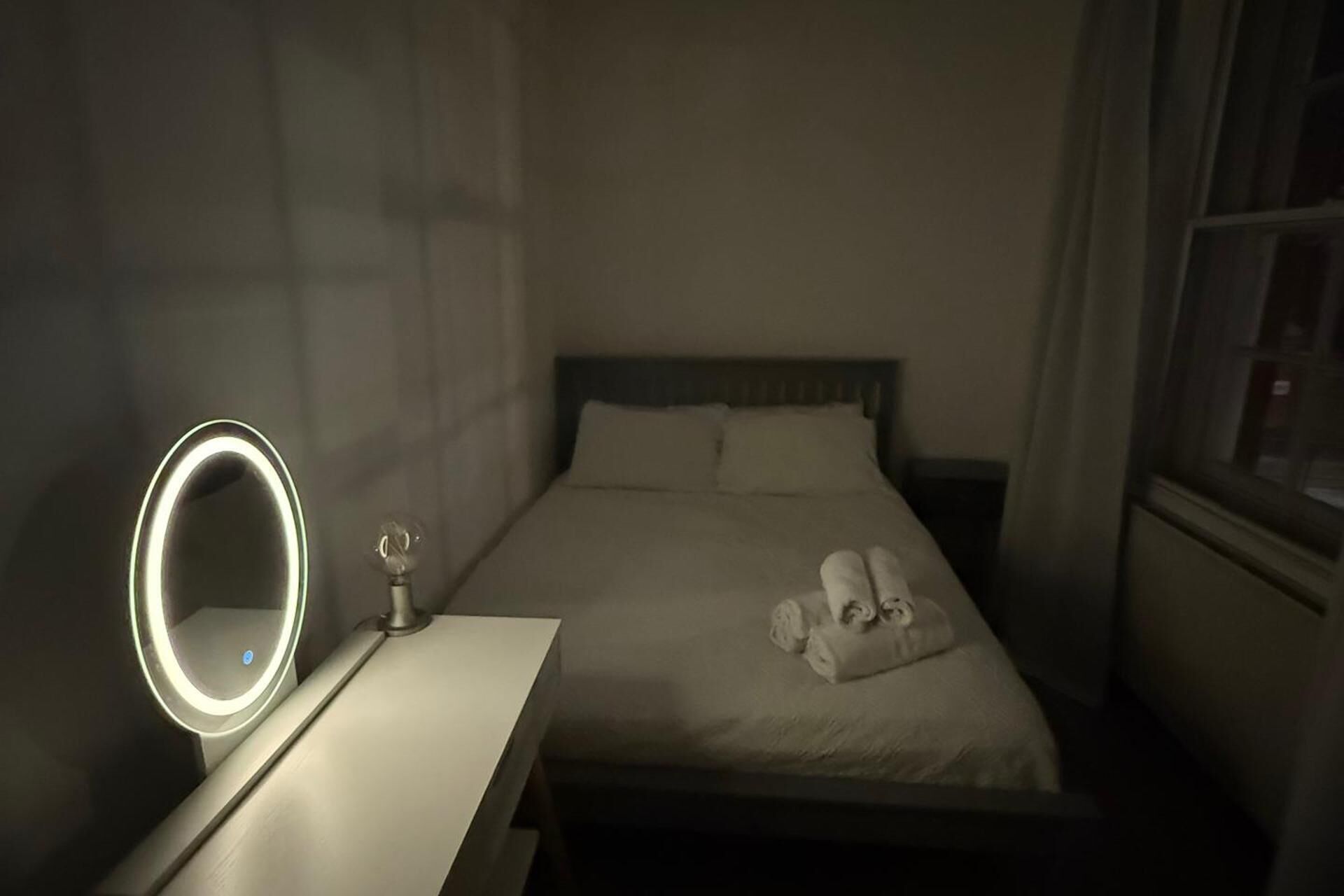 Una habitación de hotel con una cama, una mesita de noche con espejo y una ventana.