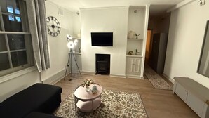 A living room with a sofa, a coffee table with flowers, a fireplace, a TV, and a clock on the wall. - Covent Garden 1-bed Apt Sleeps 4, 7 min to Station (London)