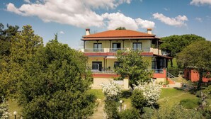 Una casa de dos pisos con techo de tejas rojas, rodeada de exuberante follaje y árboles.