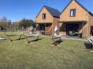 A modern building with two connected sections, each with a porch and outdoor seating. There are hammocks on the lawn. - Kalimera domki Rewal  (Rewal)