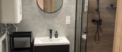 A modern bathroom with a glass-enclosed shower, a round mirror, and a black cabinet with a white sink.