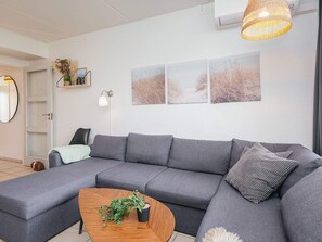 A modern living room with a grey sectional sofa, a wooden coffee table with a plant, and three framed pictures on the wall. - 5 Person Holiday Home in Ringkobing (Ringkobing)