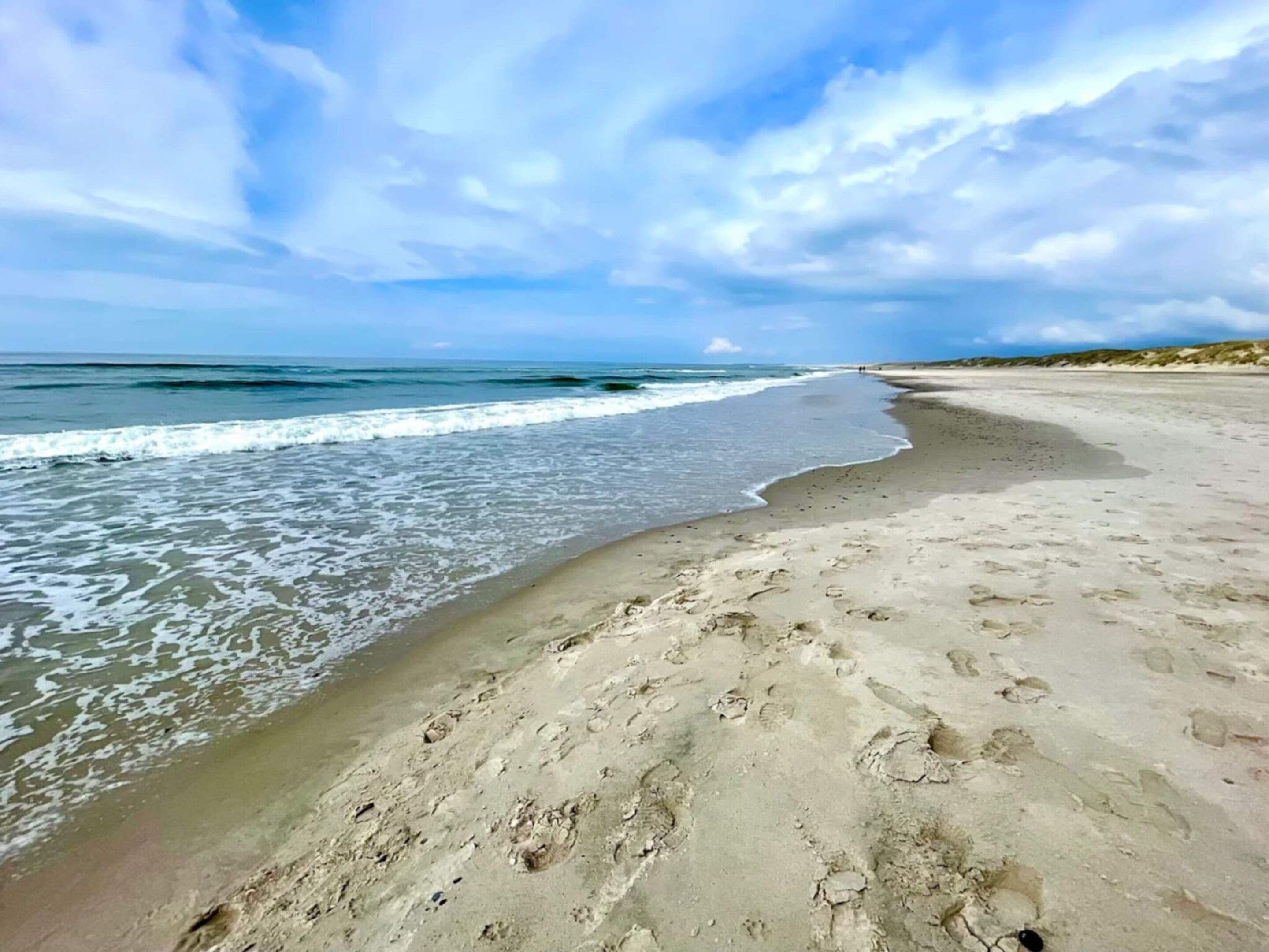 Ein Strand mit Fußabdrücken im Sand, einem klaren Himmel und Wellen, die auf das Ufer zurollen.