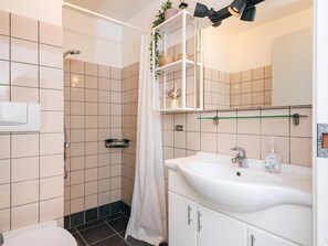A bathroom with a shower, toilet, sink, and a mirror with shelves above. - 5 Person Holiday Home in Ringkobing (Ringkobing)