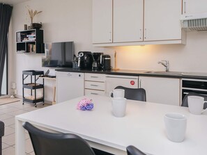 A modern kitchen with white cabinets, a coffee machine, and a dining table with chairs. - 5 Person Holiday Home in Ringkobing (Ringkobing)