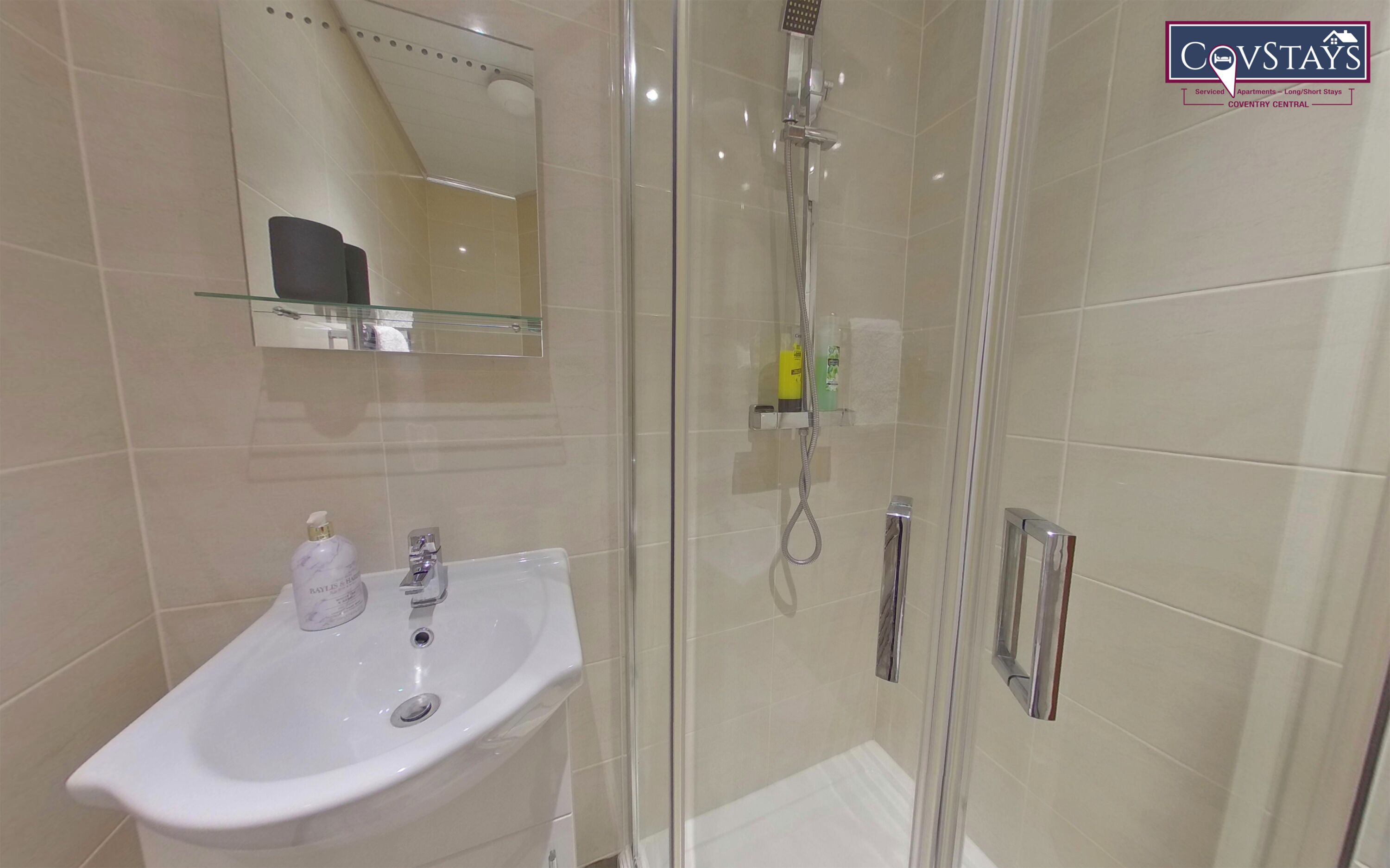 Un baño moderno con cabina de ducha de vidrio, un lavamanos blanco y un estante de vidrio sobre el lavamanos.