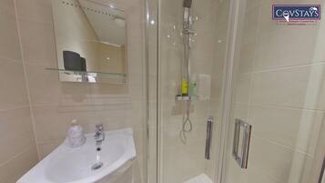 Un baño moderno con cabina de ducha de vidrio, un lavamanos blanco y un estante de vidrio sobre el lavamanos.