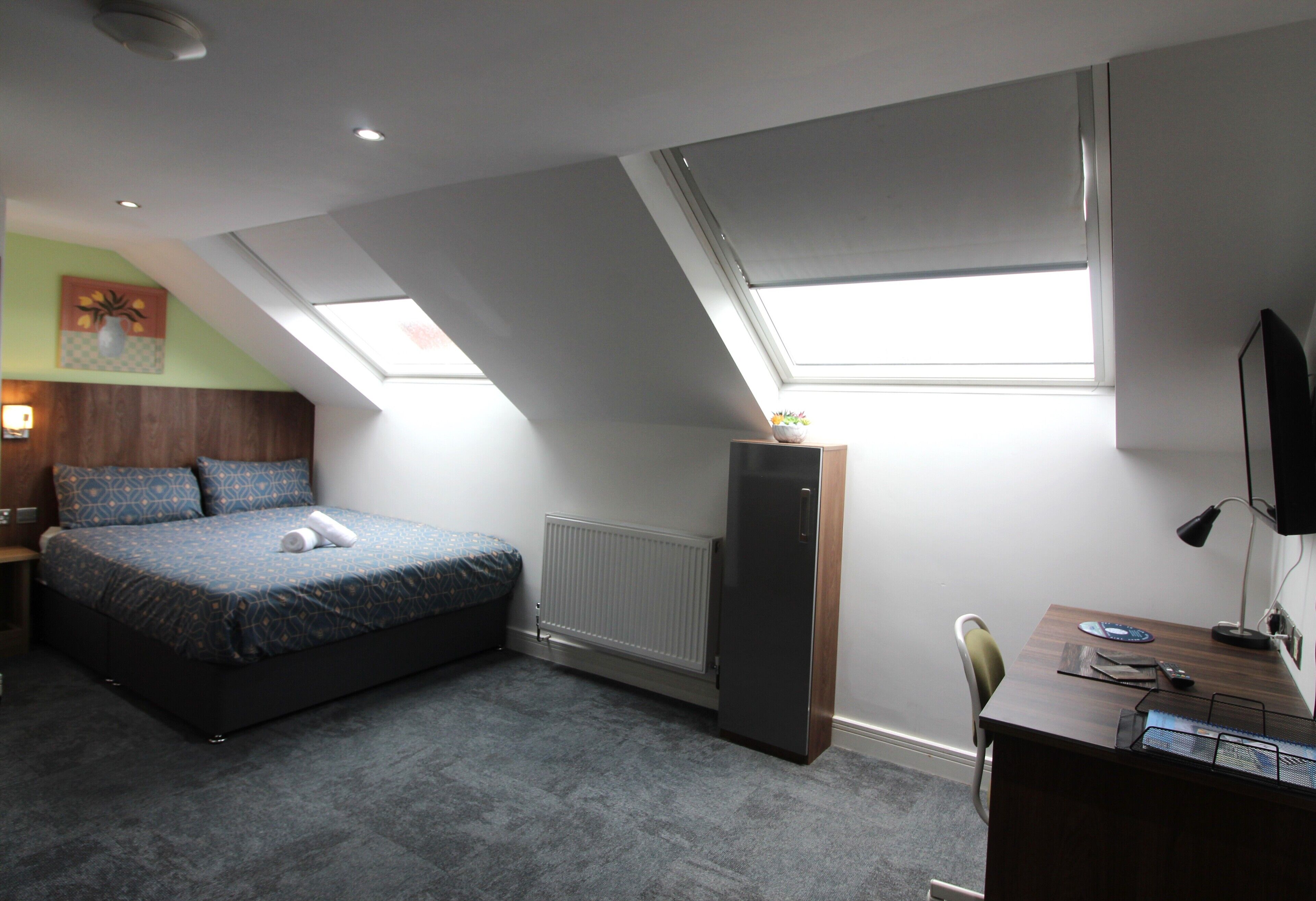 A bedroom with a bed, a desk, a radiator, and skylights.