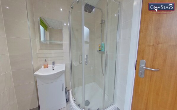 Un baño moderno con ducha envuelta en vidrio, un lavabo blanco y una puerta de madera.