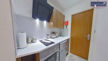 A compact kitchen with a microwave, toaster, and oven. There is a wooden door and a small shelf with items on it.