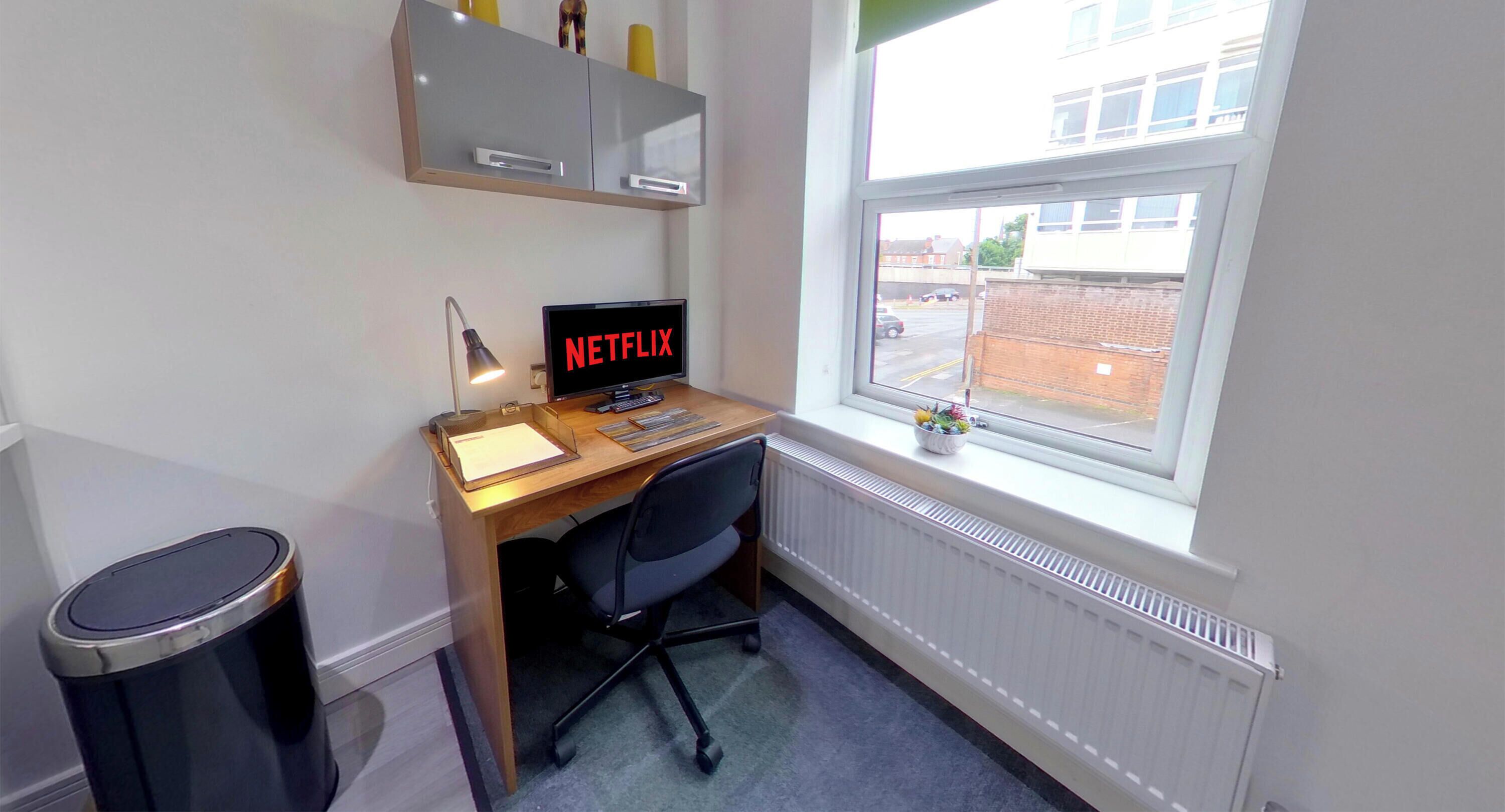 A small office space with a desk, chair, computer, and a window.