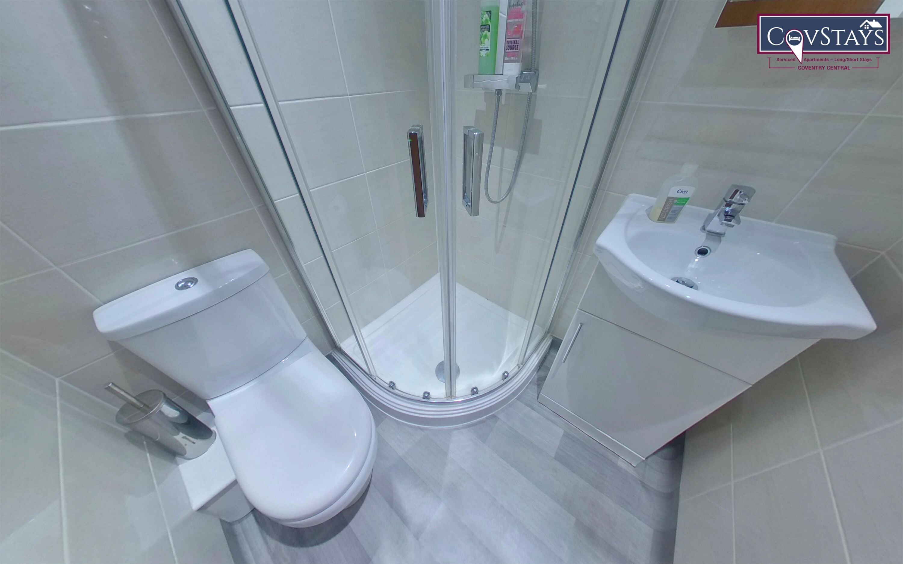 A modern bathroom with a glass-enclosed shower, a white toilet, and a sink with a soap dispenser.