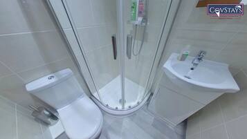A modern bathroom with a glass-enclosed shower, a white toilet, and a sink with a soap dispenser.