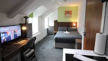 A hotel room with a bed, a desk with a computer, a chair, a window, and a door.