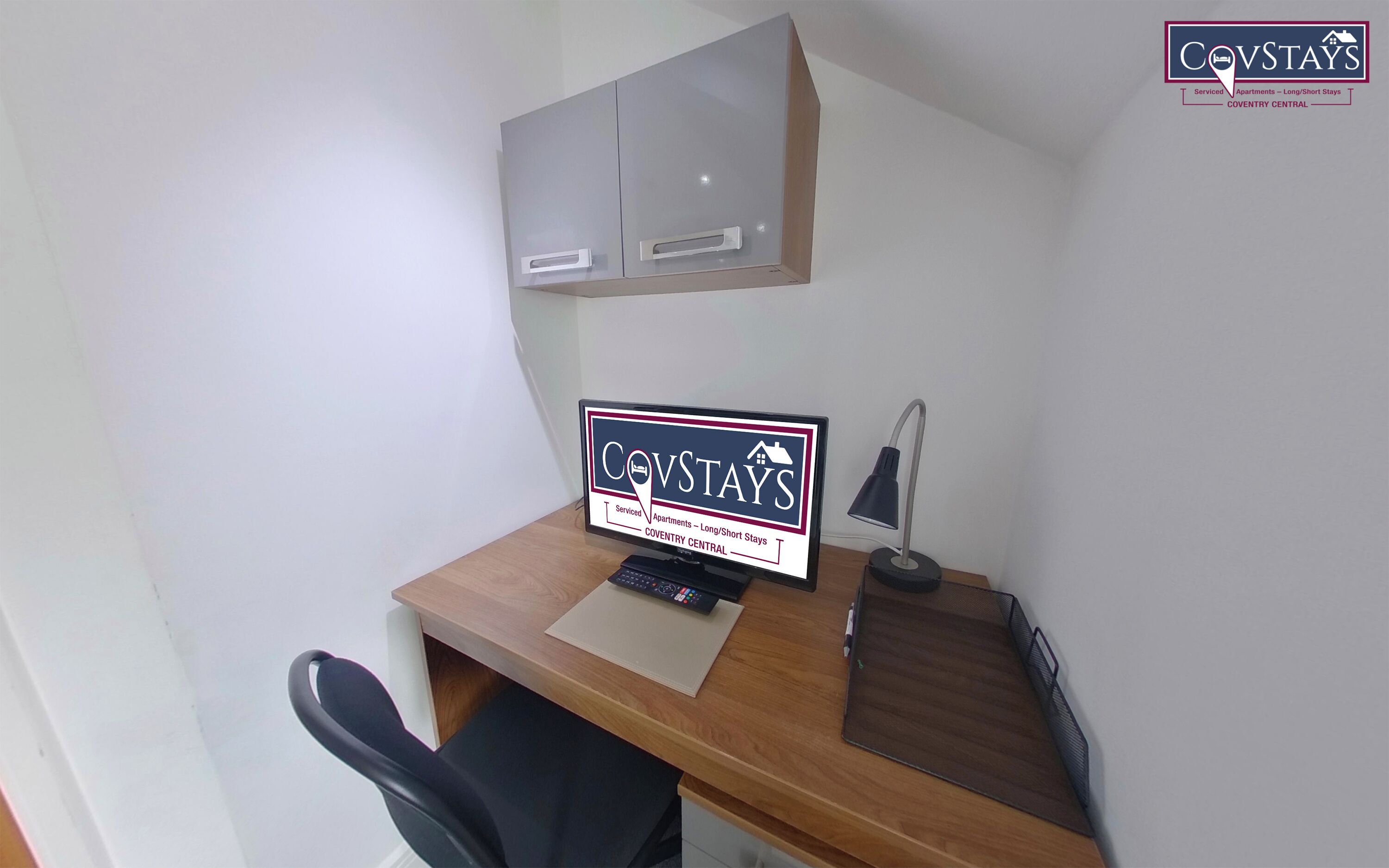 A small office space with a desk, a chair, a computer, a lamp, and a sign advertising Covstays serviced apartments in Coventry Central.