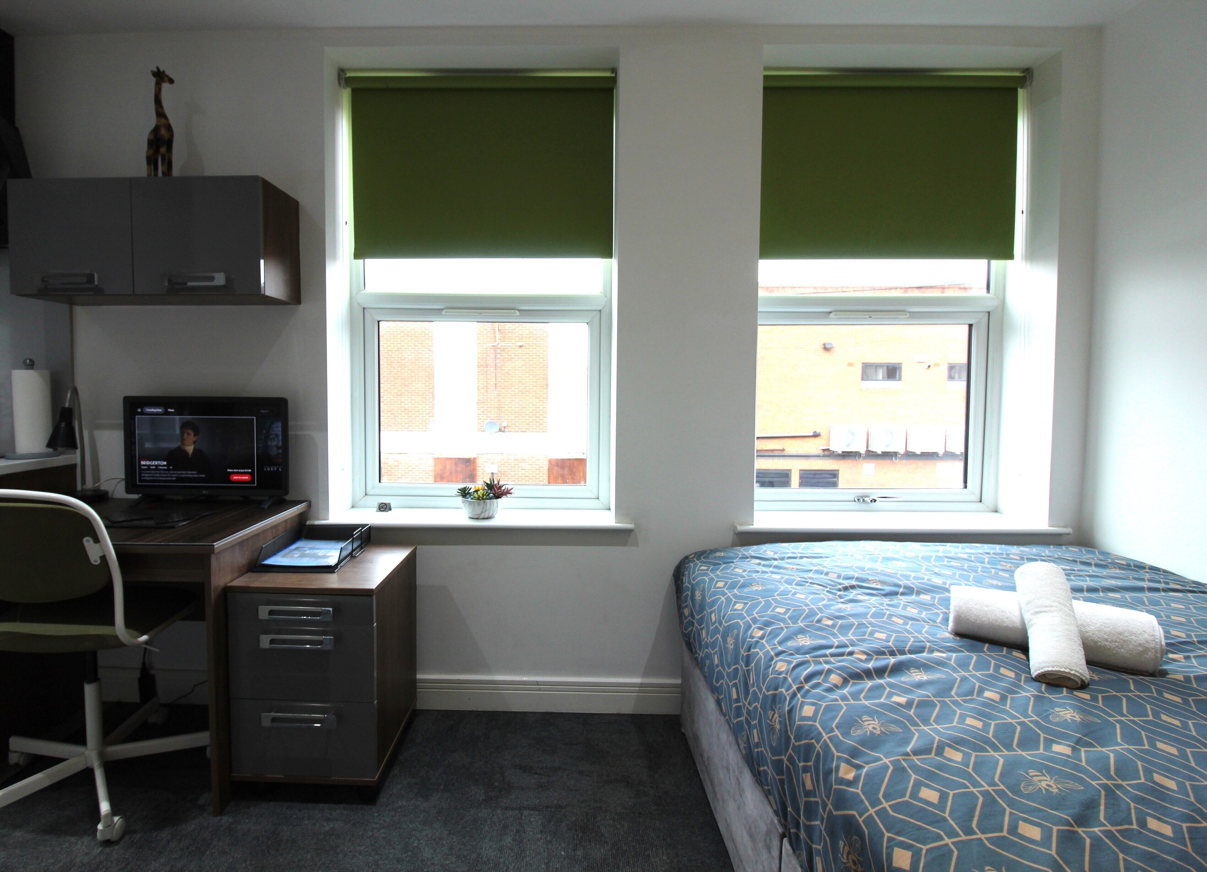 A bedroom with a desk, computer, and a bed with a patterned bedspread.
