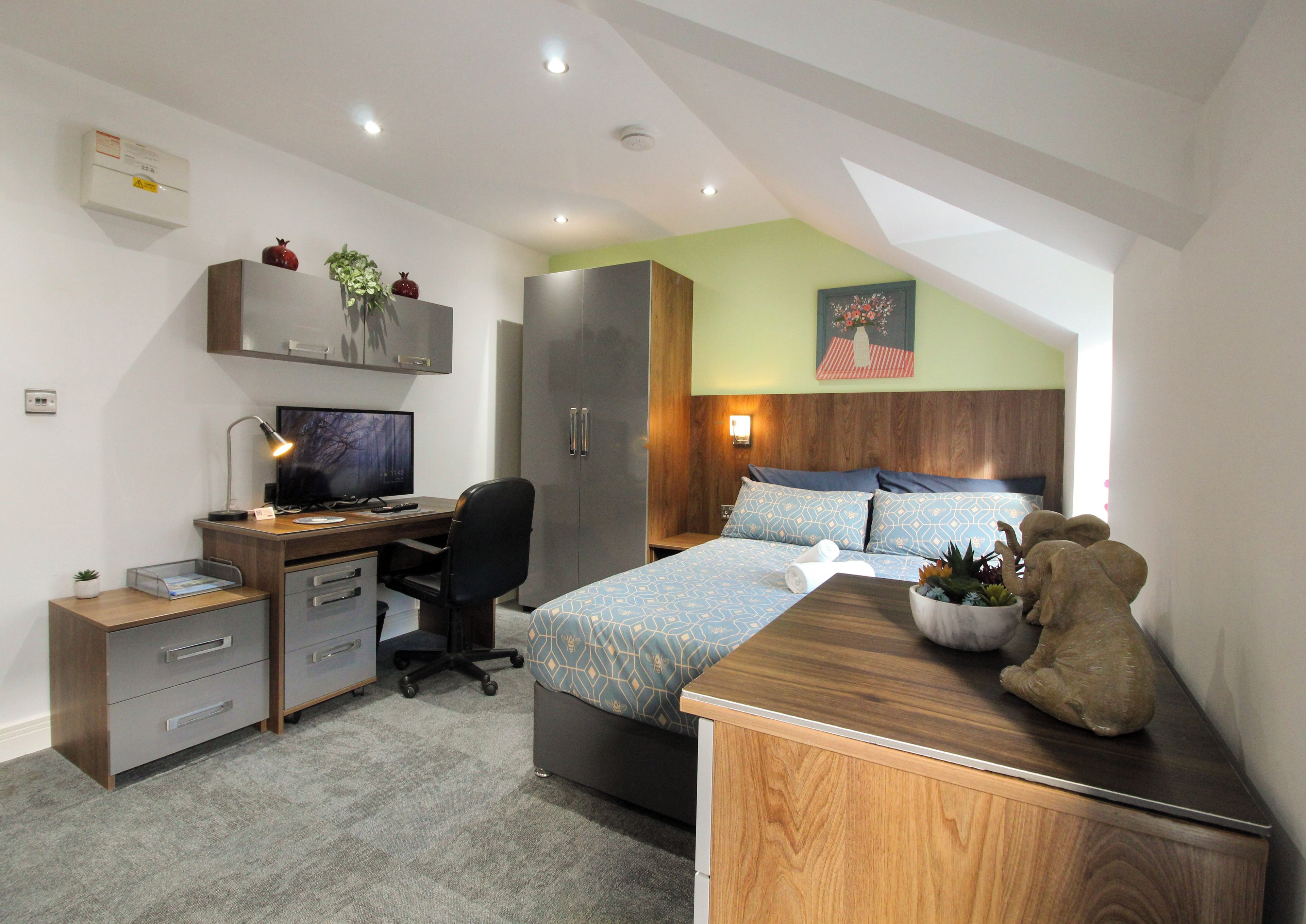 A bedroom with a desk, computer, and a bed with patterned bedding.