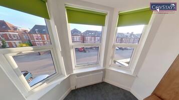 A corner room with three windows, a radiator, and a view of a residential street.