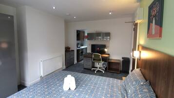 A bedroom with a bed, a desk, and a kitchenette.