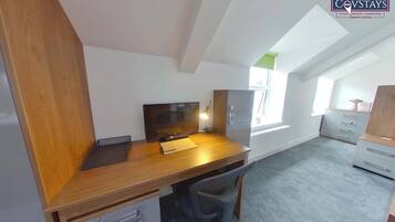 Ein modernes, helles Zimmer mit einem Holztisch, einem Computer und einem Stuhl. Ein Fenster sorgt für natürliches Licht und einen Blick nach draußen.