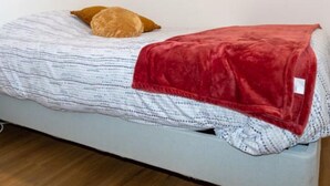 A bed with a white headboard, a red blanket, and a single brown pillow.