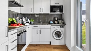 Een moderne keuken met witte kasten, een Bosch magnetron, een wasmachine en een koffiezetapparaat.