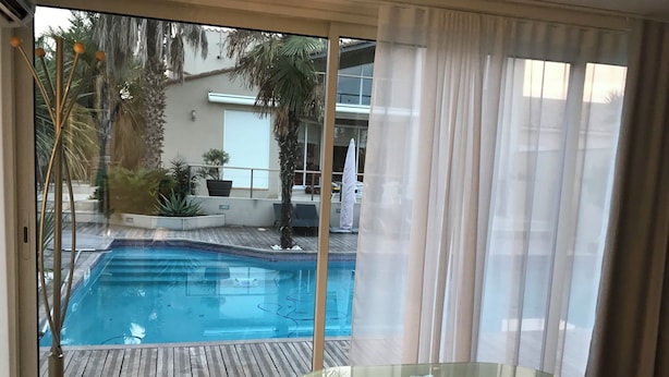 A glass-enclosed balcony with a view of a swimming pool, a wooden deck, and potted plants. - Rented T2 independent shared pool at home Near beaches. (Perpignan)