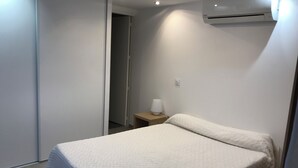 A bedroom with a bed, a nightstand, an air conditioner, and a door leading to another room. - Rented T2 independent shared pool at home Near beaches. (Perpignan)