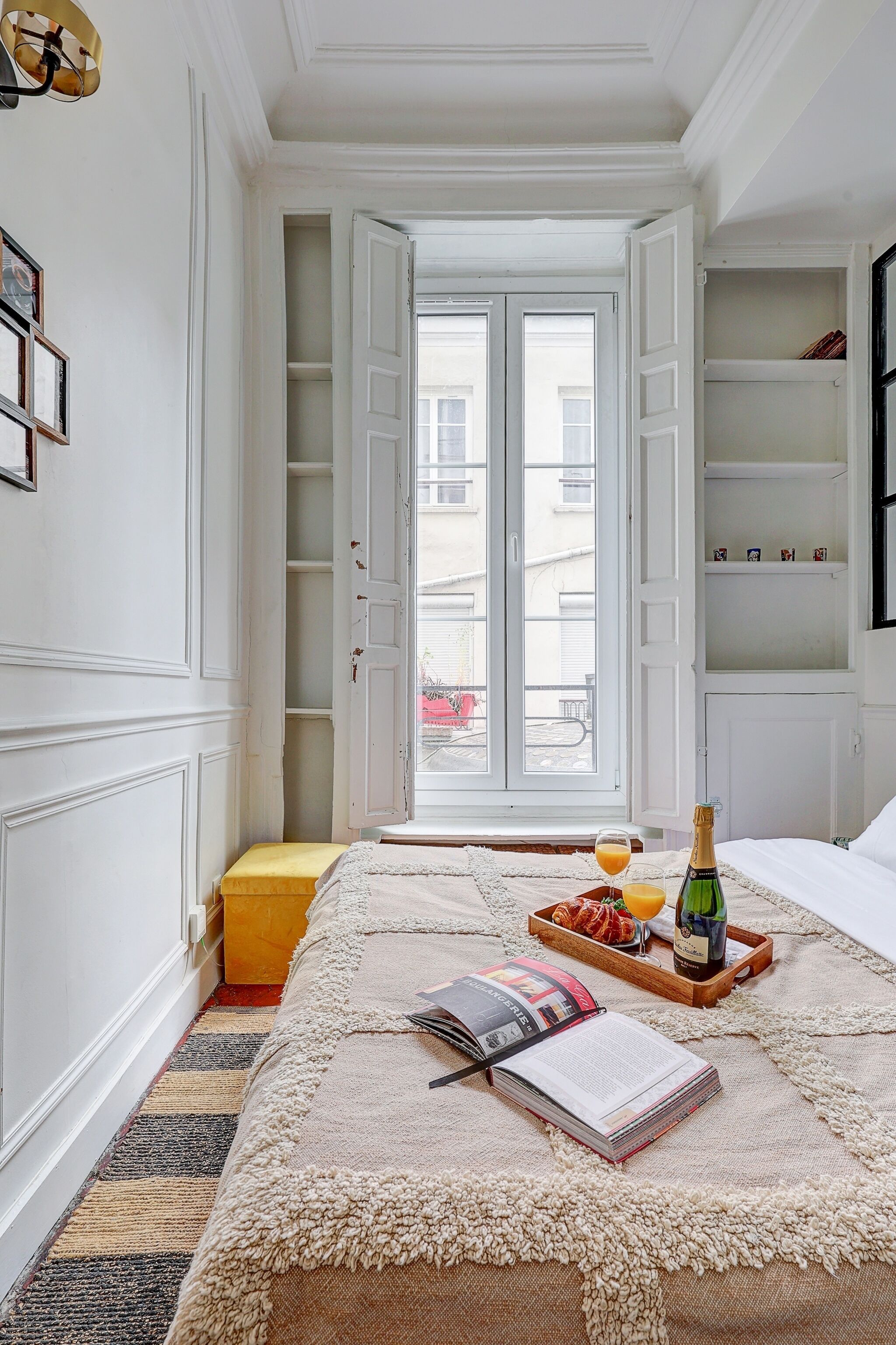 Une chambre avec un lit, une fenêtre donnant sur un beau paysage, une étagère avec des objets décoratifs et un plateau avec une bouteille et des verres.