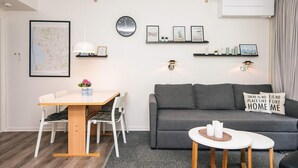 A modern living room with a sofa, a dining table with chairs, a small round table with candles, a wall clock, framed pictures, and a map on the wall. - 4 Person Holiday Home in Ringkobing (Ringkobing)