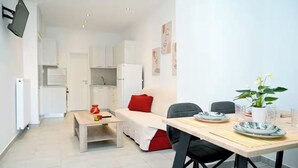 A compact living space with a kitchenette, a dining area with a table set for two, and a sofa with red cushions.