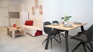 A modern living room with a dining area, a kitchenette, and a red accent pillow on the sofa.
