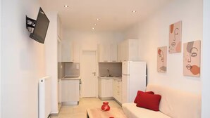 A compact living space with a kitchenette, a sofa with a red pillow, and wall art.
