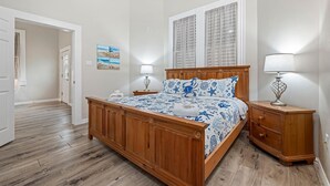 Un dormitorio con cama de madera, mesitas de noche, una ventana con cortinas y un pasillo.