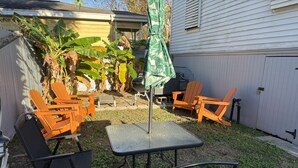 Een buitenpatio met een tafel, stoelen, een barbecue en een overdekte parasol.