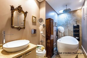 Un baño con un lavamanos ovalado grande, un inodoro independiente, un tocador con espejo y una ducha con cabezal de lluvia.