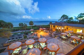 Un resort frente a la playa con zonas de comedor al aire libre, sombrillas y vistas al océano.