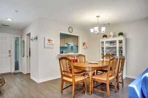 Un comedor con una mesa redonda de madera y seis sillas, una araña y un armario blanco con objetos decorativos.