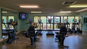 Ein Fitnessstudio mit Laufbändern, Crosstrainern und einem Fernseher an der Wand.