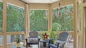 Egy üvegfallal rendelkező, világos helyiség, melyben két Adirondack-stílusú szék, egy kis, kerek asztal és egy díszes csillár található.