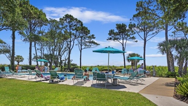 Un espace aménagé au bord de la piscine, avec des chaises longues vertes et des parasols, le tout entouré de grands arbres.