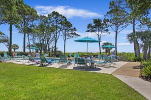 A poolside area with green lounge chairs and umbrellas, surrounded by tall trees. - How You Dune? - Beachwood Place 2 Bedroom Condo (Hilton Head Island)