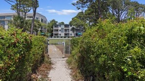 Un chemin mène à une zone délimitée par une grille, avec un bâtiment visible au loin.