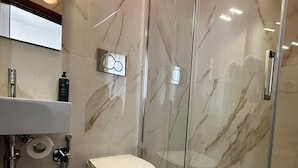 Une salle de bain moderne avec un sol en marbre, des toilettes, une douche en verre et un lavabo avec un miroir au-dessus.