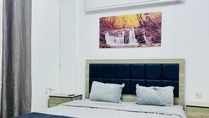 Een net opgemaakt bed met een hoofdbord, een aan de muur bevestigde airconditioner en een schilderij van een waterval.