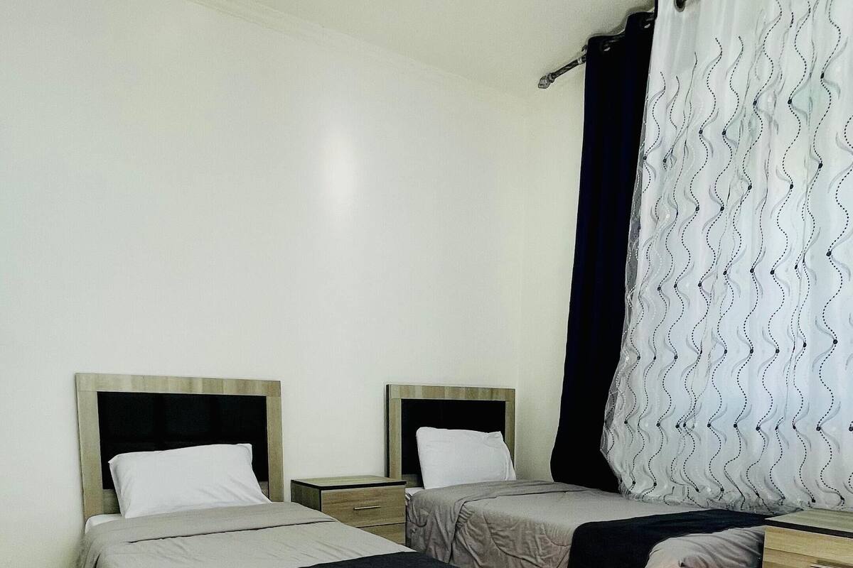 Une chambre d’hôtel avec deux lits, une table de chevet, une commode et un rideau à motifs ondulés.